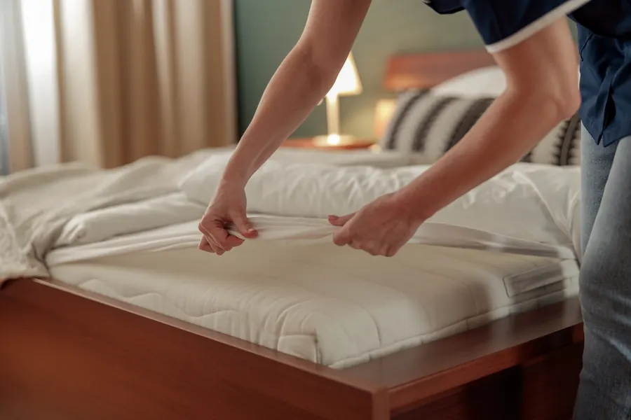 Manos tendiendo la cama con lencería blanca en una habitación cálida